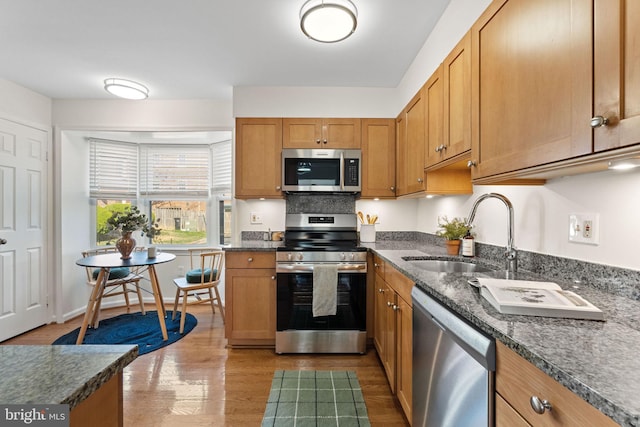 kitchen featuring wood finished floors, stainless steel appliances, dark stone counters, and a sink