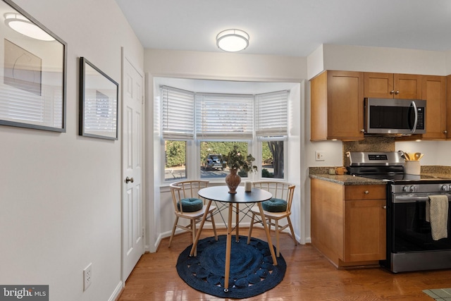 kitchen featuring brown cabinetry, baseboards, stainless steel appliances, and light wood-style floors