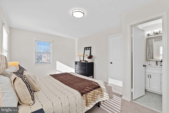 bedroom with baseboards, ensuite bathroom, and light carpet