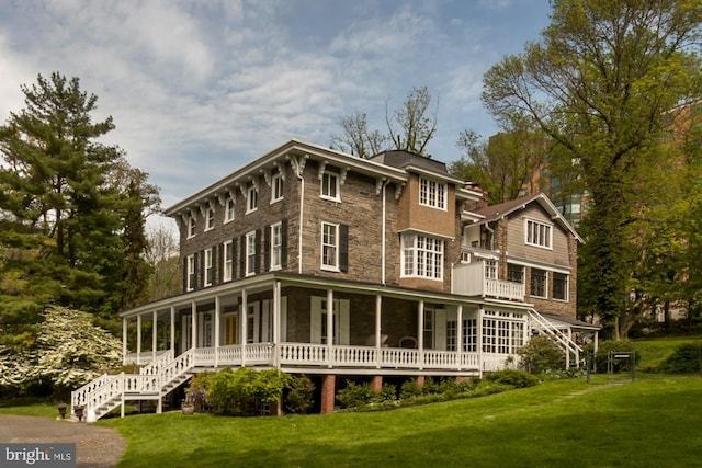 rear view of house with stairway, a yard, and stone siding