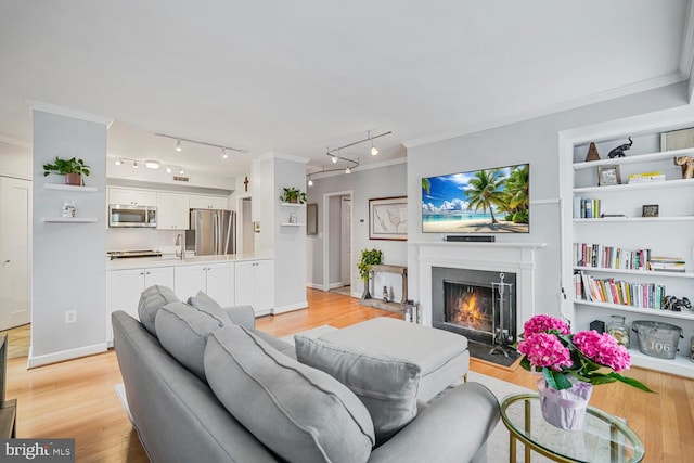 living area with built in features, a fireplace with flush hearth, light wood-style floors, and crown molding