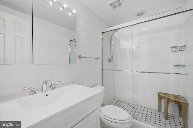 bathroom featuring tile walls, toilet, visible vents, and a stall shower