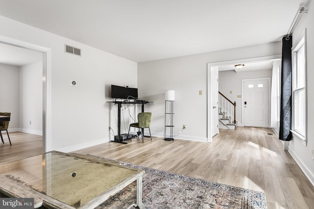 living area featuring stairs, baseboards, visible vents, and light wood-type flooring