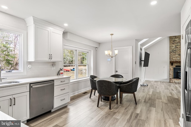 kitchen featuring white cabinetry, a sink, decorative backsplash, dishwasher, and light wood-type flooring