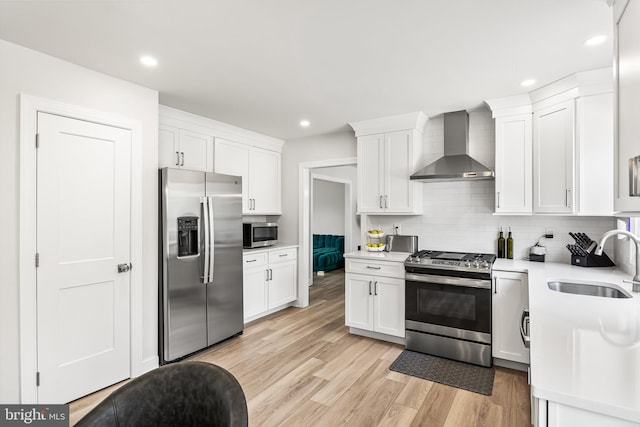 kitchen with a sink, decorative backsplash, light countertops, appliances with stainless steel finishes, and wall chimney exhaust hood