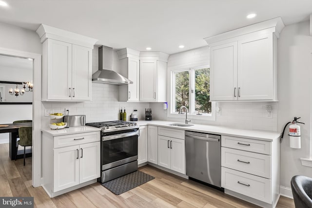 kitchen with white cabinetry, wall chimney range hood, a sink, and stainless steel appliances