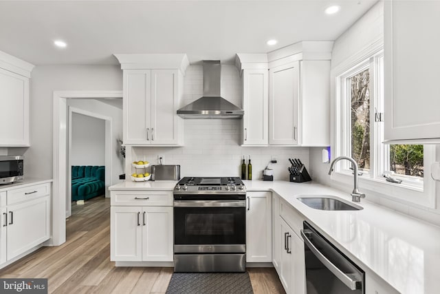 kitchen featuring light wood finished floors, a sink, decorative backsplash, appliances with stainless steel finishes, and wall chimney exhaust hood