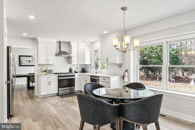 kitchen with a notable chandelier, backsplash, appliances with stainless steel finishes, and wall chimney exhaust hood