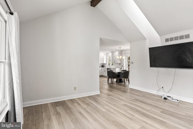 unfurnished living room with baseboards, visible vents, light wood finished floors, beamed ceiling, and a notable chandelier