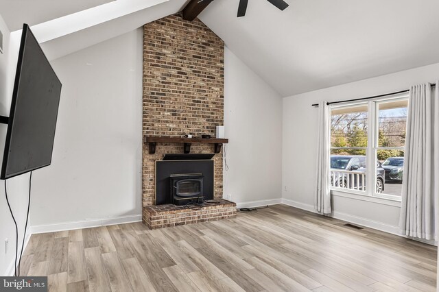 unfurnished living room with wood finished floors, visible vents, lofted ceiling with beams, a wood stove, and ceiling fan