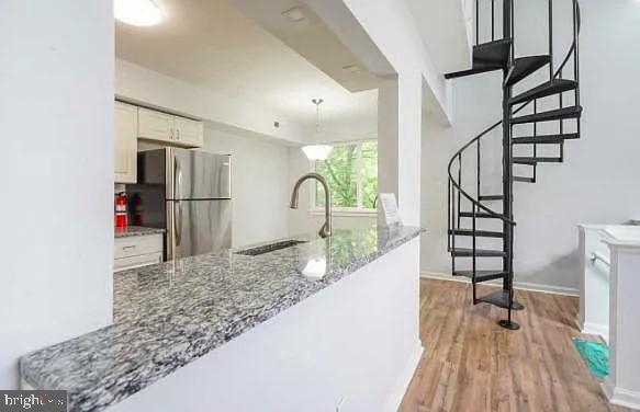 kitchen with light wood finished floors, decorative light fixtures, stone counters, freestanding refrigerator, and white cabinets