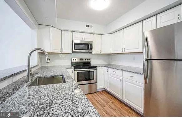 kitchen featuring visible vents, light stone countertops, white cabinets, stainless steel appliances, and a sink