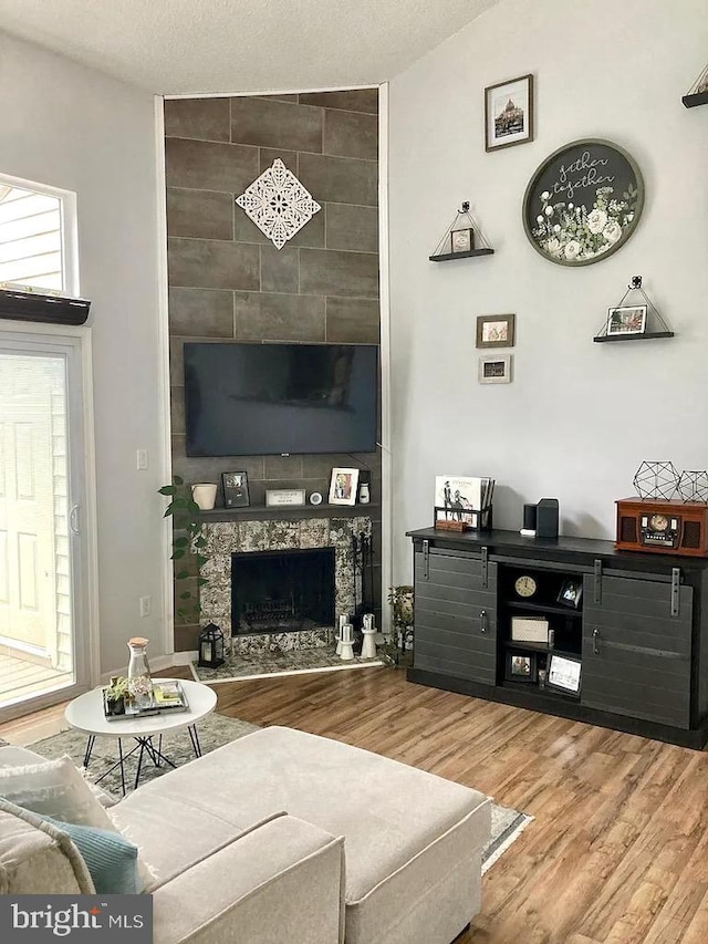 living room with a tiled fireplace, wood finished floors, and a textured ceiling