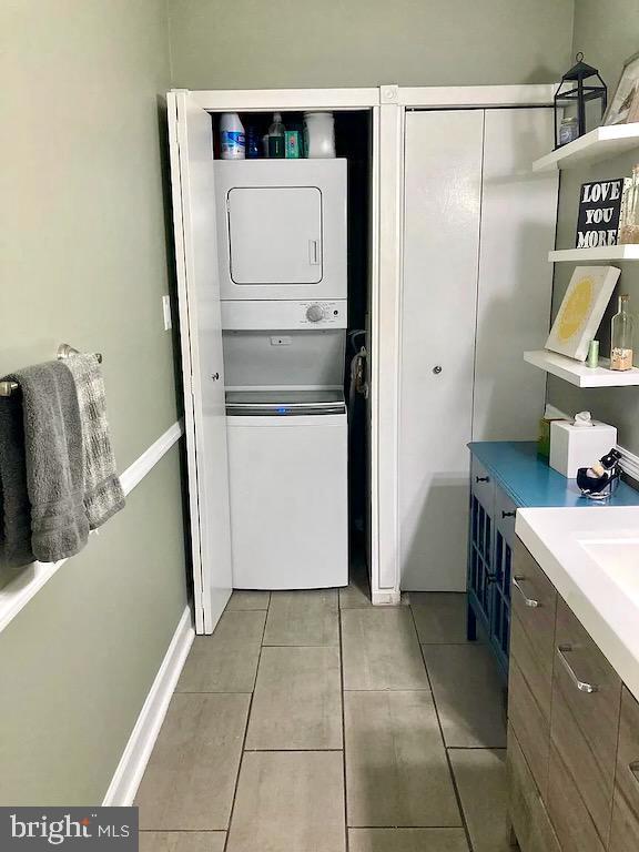 laundry room featuring laundry area, light tile patterned floors, baseboards, and stacked washer and clothes dryer