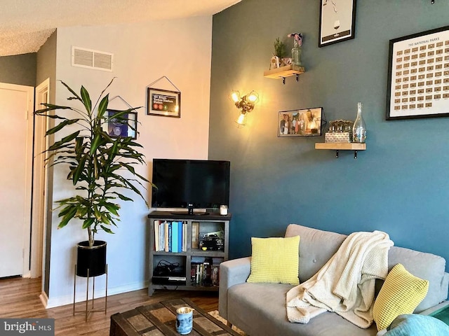 living room with visible vents, lofted ceiling, baseboards, and wood finished floors