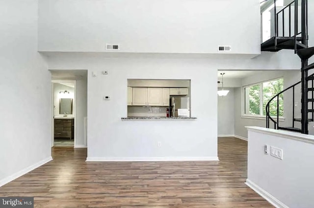 unfurnished living room featuring visible vents, baseboards, dark wood-style floors, and stairs