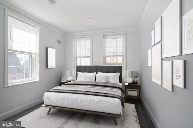 bedroom with visible vents, baseboards, wood finished floors, and crown molding