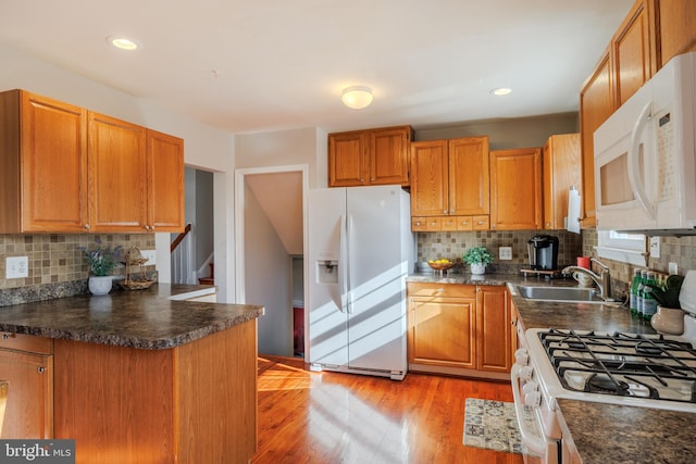 kitchen featuring dark countertops, white appliances, light wood-type flooring, and a sink