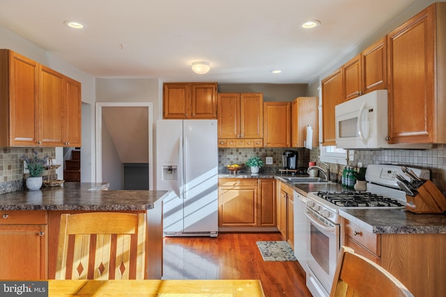 kitchen featuring white appliances, brown cabinetry, a sink, light wood-style floors, and dark countertops