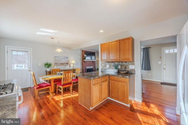 kitchen with pendant lighting, dark countertops, backsplash, wood finished floors, and a peninsula