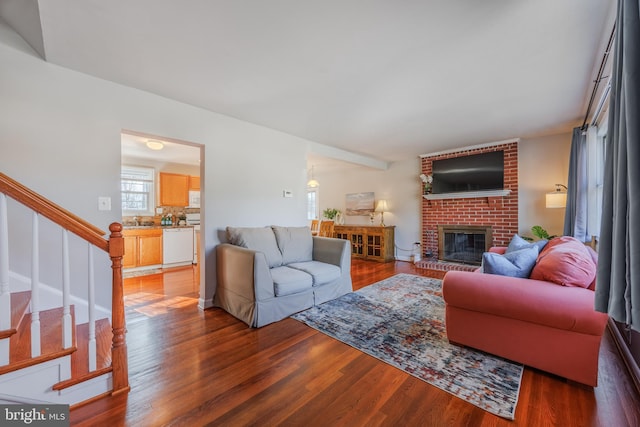 living room featuring stairs, a brick fireplace, and wood finished floors