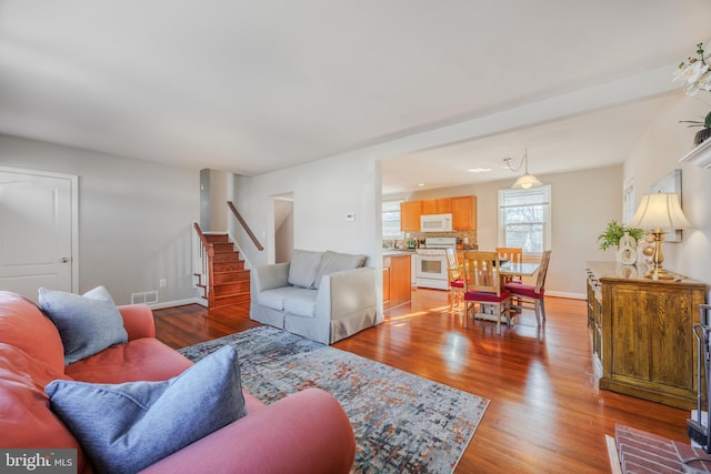 living room featuring stairway, wood finished floors, visible vents, and baseboards