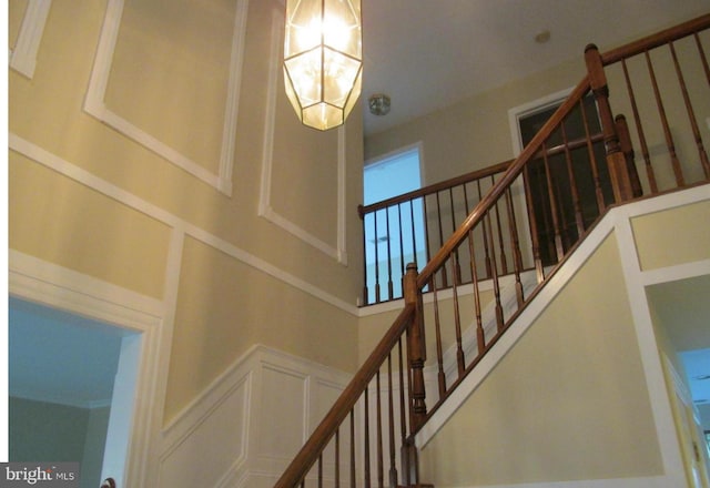 stairway with a notable chandelier, wainscoting, and a decorative wall