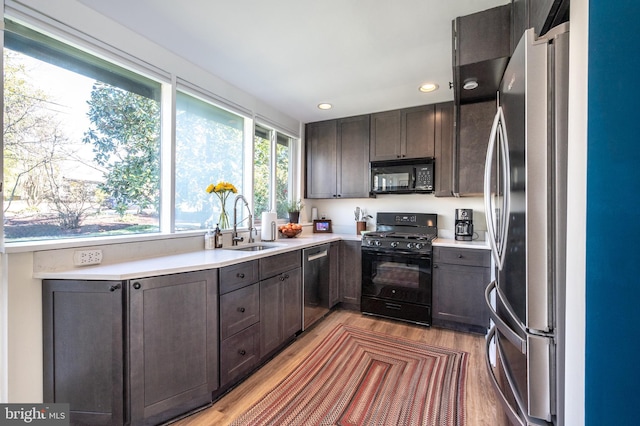 kitchen featuring a sink, black appliances, light wood-style flooring, and light countertops