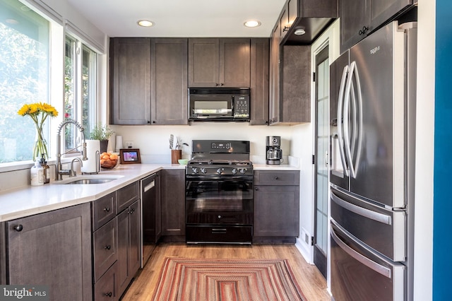 kitchen featuring a sink, black appliances, dark brown cabinetry, light countertops, and light wood-style floors