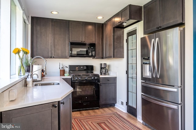 kitchen with light wood-type flooring, black appliances, a sink, light countertops, and dark brown cabinets