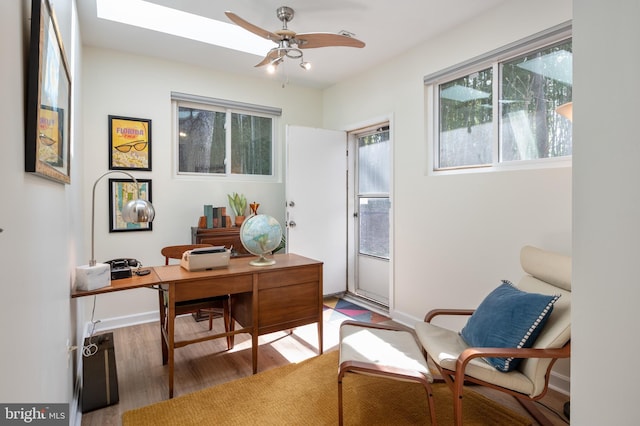 office area with ceiling fan, baseboards, wood finished floors, and a skylight