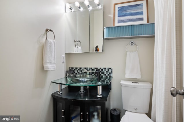 bathroom featuring toilet, backsplash, and a sink