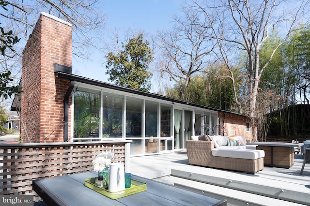 rear view of house featuring a deck, a sunroom, and a chimney