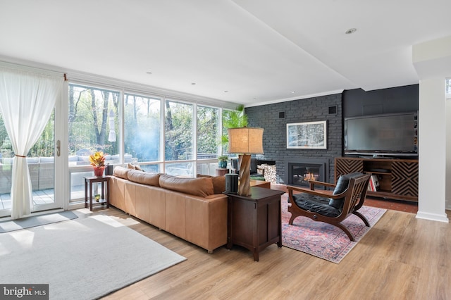 living area with a wealth of natural light, ornamental molding, a brick fireplace, and wood finished floors