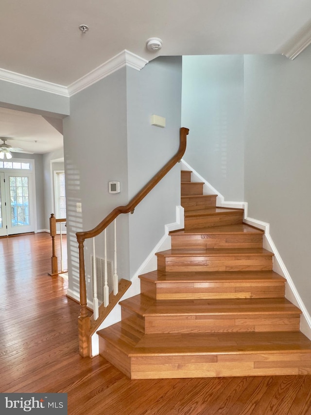 stairway with a ceiling fan, crown molding, baseboards, and wood finished floors