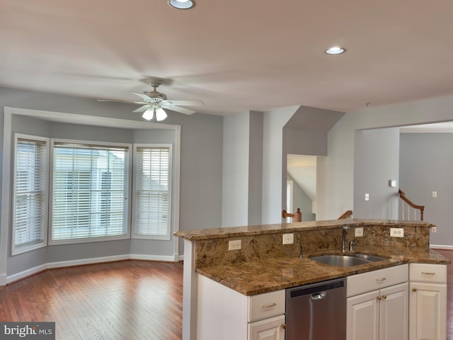 kitchen featuring a sink, hardwood / wood-style floors, dark stone counters, baseboards, and dishwasher