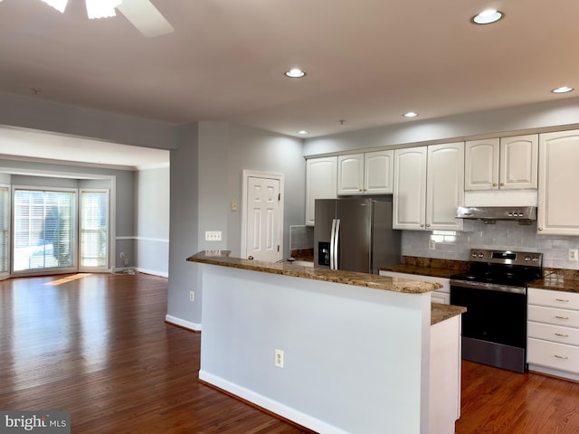 kitchen with under cabinet range hood, dark stone counters, decorative backsplash, appliances with stainless steel finishes, and dark wood-style flooring