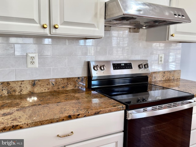 kitchen with stainless steel electric range oven, dark stone counters, under cabinet range hood, white cabinetry, and tasteful backsplash