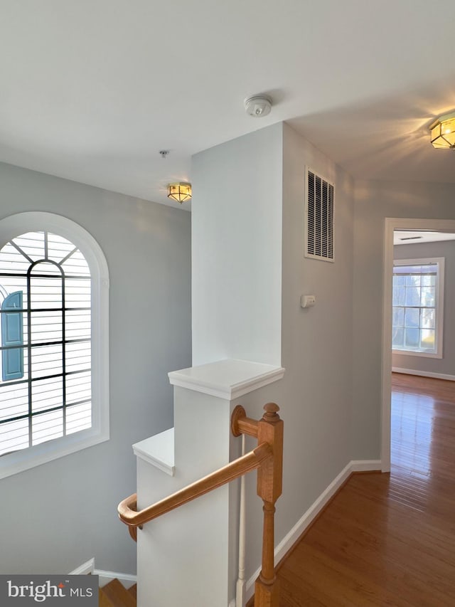 hallway with an upstairs landing, wood finished floors, visible vents, and baseboards