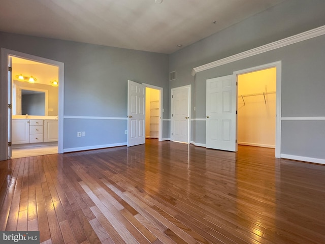 unfurnished bedroom with visible vents, baseboards, a walk in closet, and hardwood / wood-style flooring