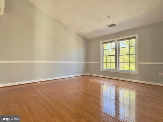 empty room with visible vents, lofted ceiling, baseboards, and hardwood / wood-style flooring