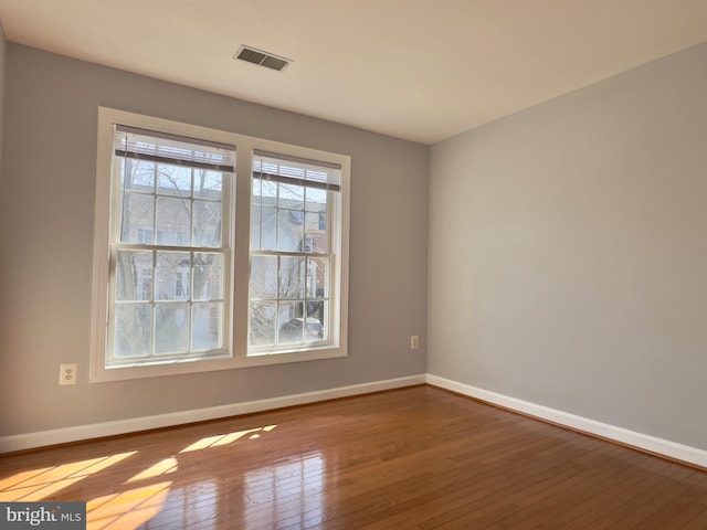 unfurnished room with hardwood / wood-style flooring, baseboards, and visible vents