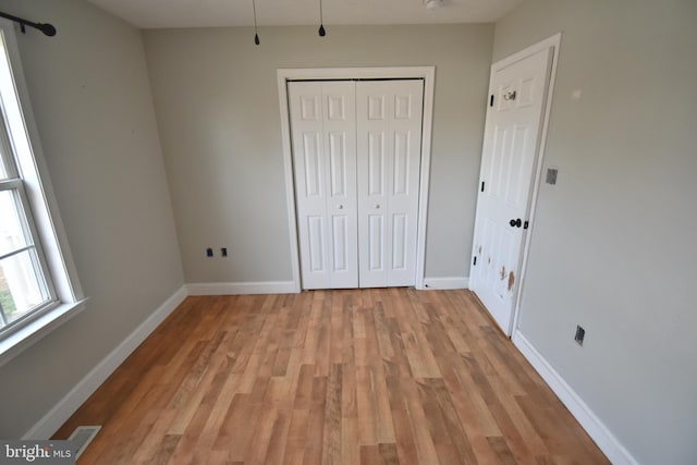 unfurnished bedroom featuring baseboards, light wood-type flooring, and a closet