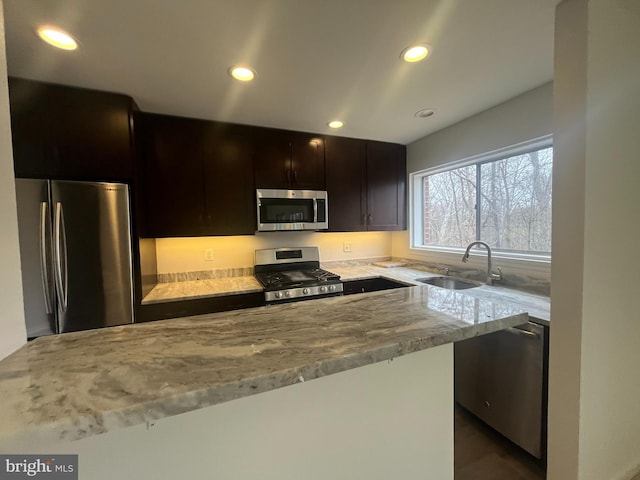 kitchen with light stone counters, recessed lighting, a sink, dark brown cabinetry, and appliances with stainless steel finishes