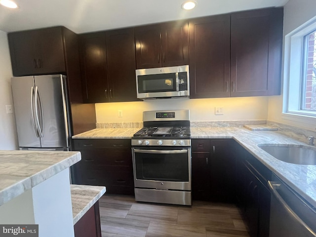 kitchen featuring dark brown cabinetry, light stone counters, recessed lighting, stainless steel appliances, and a sink