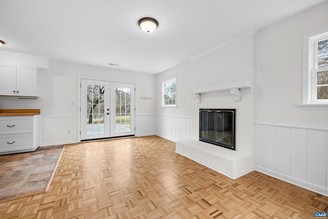 unfurnished living room featuring french doors, a brick fireplace, wainscoting, and visible vents