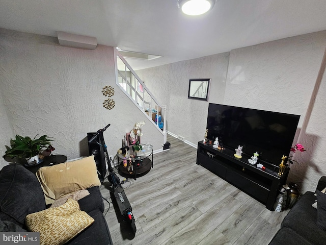 living room featuring baseboards, wood finished floors, stairs, and a textured wall