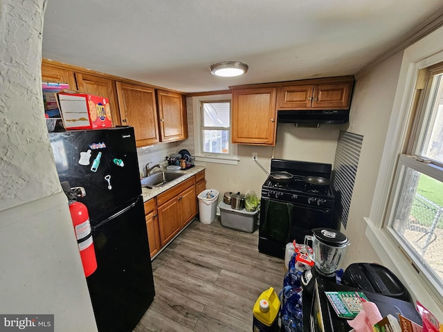 kitchen with under cabinet range hood, brown cabinets, black appliances, and light wood-style floors