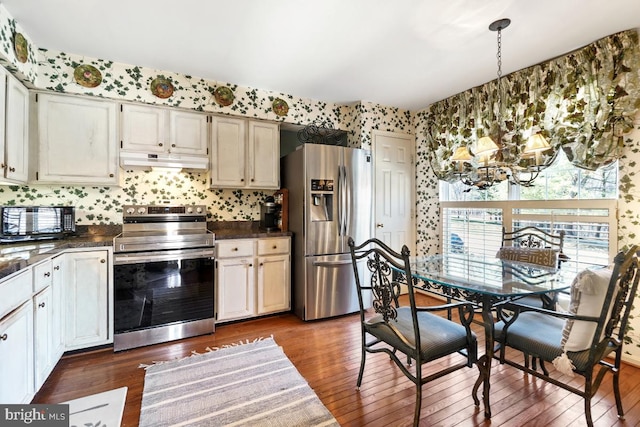 kitchen with under cabinet range hood, wallpapered walls, stainless steel appliances, and dark countertops