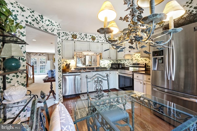 kitchen featuring dark wood finished floors, wallpapered walls, a sink, appliances with stainless steel finishes, and dark countertops